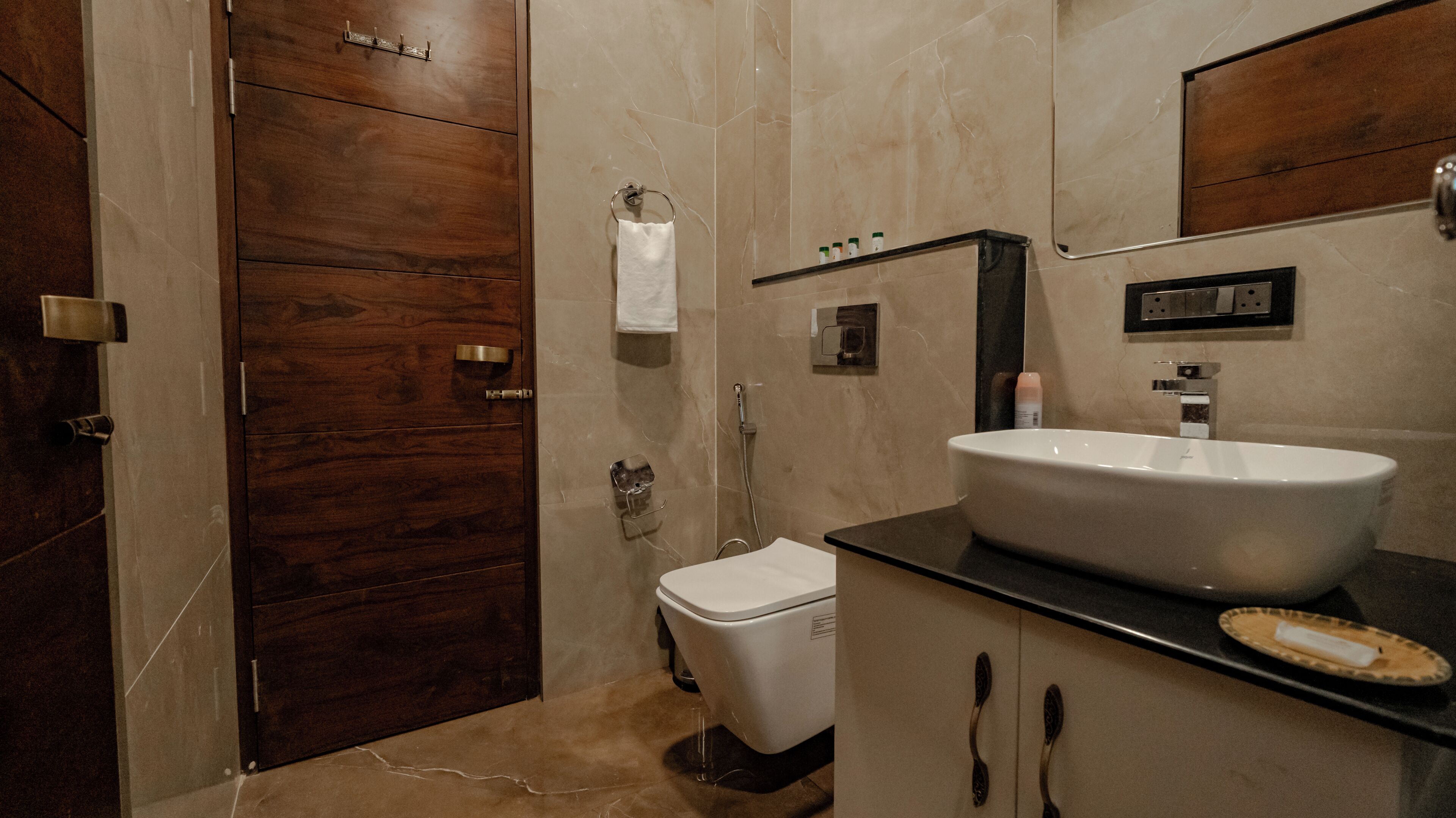 Een badkamer met een houten deur, een wit toilet, een wastafel met spiegel en een douche.