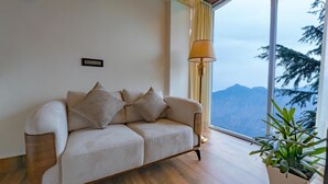 Un soggiorno moderno con un divano, una lampada da terra e vista sulle montagne attraverso un'ampia finestra.