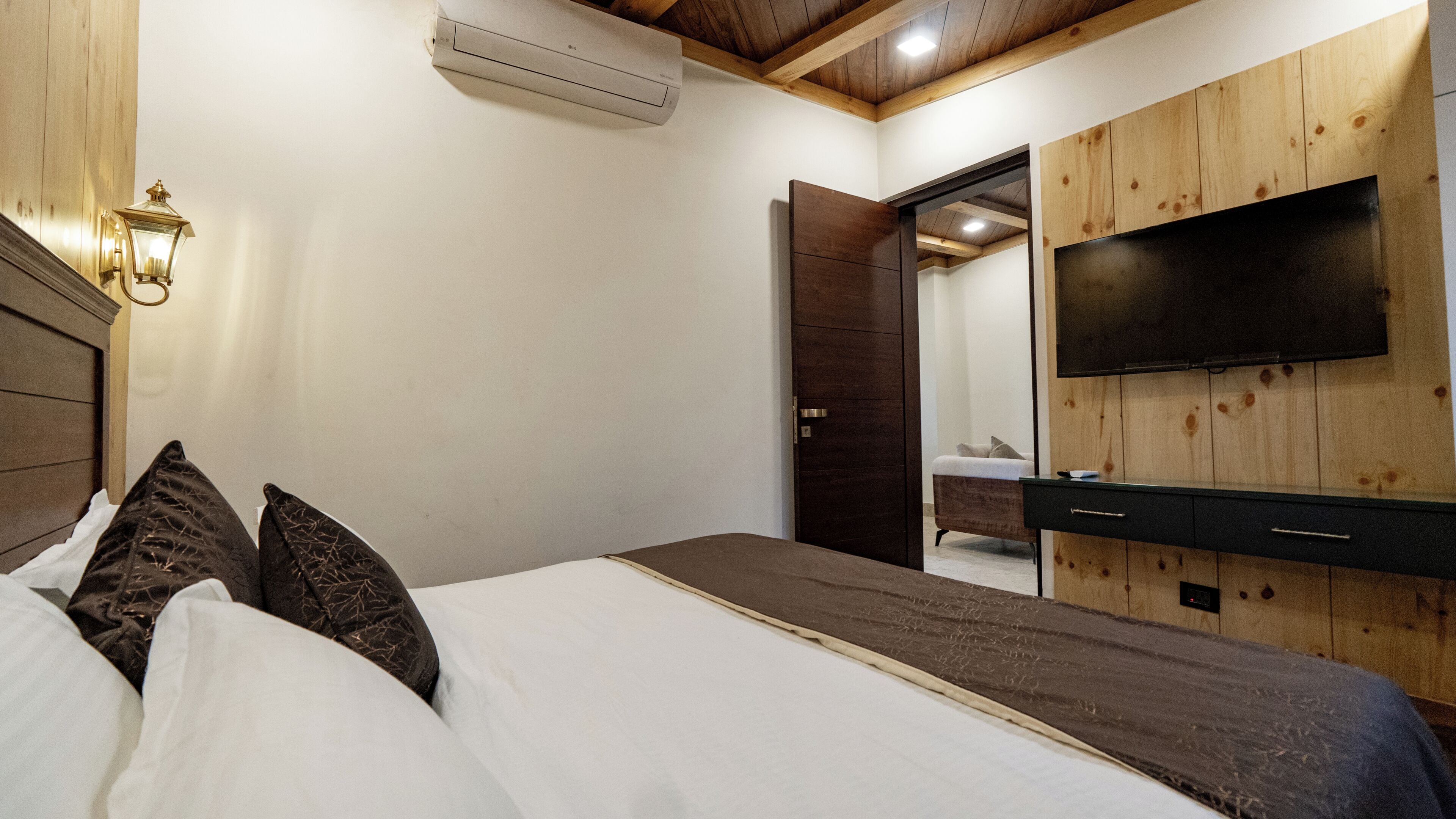 A bedroom with a bed, a bedside table, a TV mounted on a wooden wall, and an air conditioning unit.