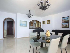 Uma sala de jantar com mesa de vidro, quatro cadeiras, um candelabro e obras de arte penduradas na parede.