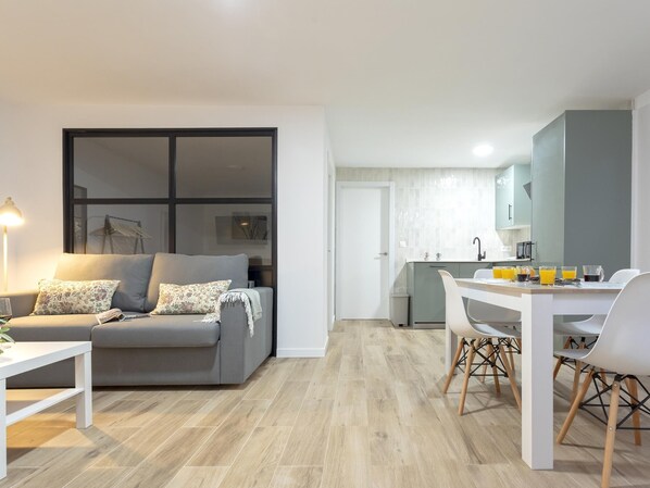 A modern living room with a grey sofa, a white coffee table, and a dining area with a white table and chairs.