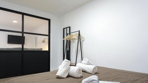 A hotel room with a large bed, a wooden floor, a black wardrobe, a TV on the wall, and a towel rack with towels.