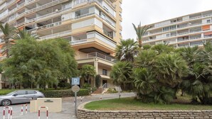 A multi-story residential building with balconies, a parking sign, and a stone wall.