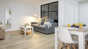 A modern living room with a grey sofa, a white coffee table, and a dining area with a wooden table and white chairs.