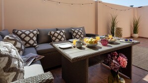 Un espace extérieur aménagé avec une table en osier, des coussins et une plante en pot.