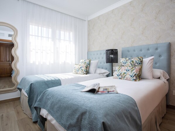 Una habitación de hotel con dos camas, un espejo grande y una ventana con cortinas traslúcidas.
