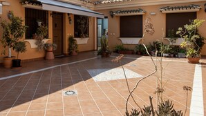 Une cour avec un sol carrelé, des plantes en pot et un espace détente abrité.
