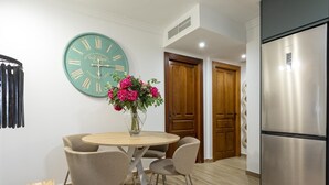 Une cuisine moderne avec un réfrigérateur en acier inoxydable, une horloge murale de couleur turquoise et une table à manger en bois avec des chaises.