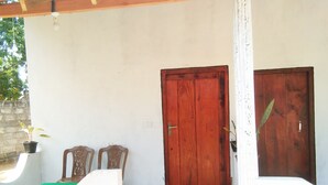 A room with a wooden door, two chairs, a small potted plant, and a green mat on the floor.