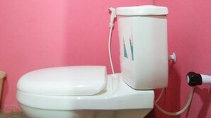 A toilet with a white tank and seat, connected to a white pipe, in a room with pink walls.