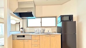 A compact kitchen with wooden cabinets, a black refrigerator, a microwave, and a dishwasher. - FuranoBnB (Furano)