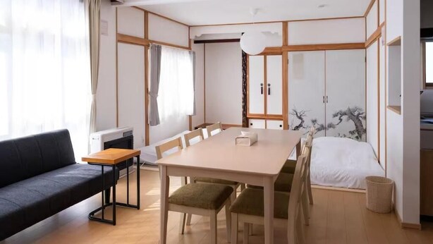 A modern room with a wooden dining table, a sofa, and a bed. - FuranoBnB (Furano)