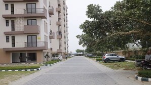 A residential building with multiple balconies, a paved walkway, and parked cars.