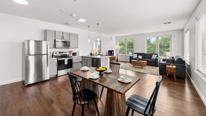 Eine moderne Küche mit Edelstahlgeräten, ein Essbereich mit Holztisch und -stühlen sowie ein Wohnzimmer mit Sofa und Couchtisch.