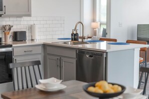 Moderni keittiö, jossa on sisäänrakennettu astianpesukone, pesuallas sekä ruokailutila pöydän ja tuolien kera.
