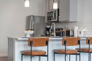 Keittiössä on keskellä sijaitseva saareke, baarituoleja, hedelmäkulho ja modernit kodinkoneet.