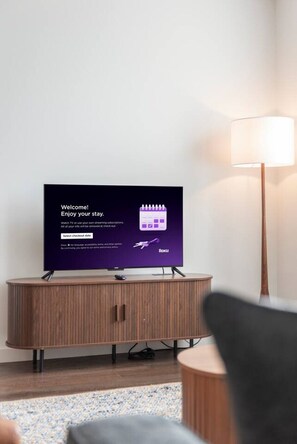 Televisiossa näkyy tervetuliaisviesti ja Roku-logo, mikä viittaa siihen, että hotellihuoneessa on käytössä älytelevisio. Huoneessa on myös puinen kaappi ja lamppu.