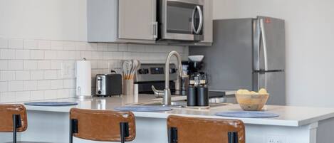 Cozinha moderna com ilha central, eletrodomésticos de aço inoxidável e banquetas.