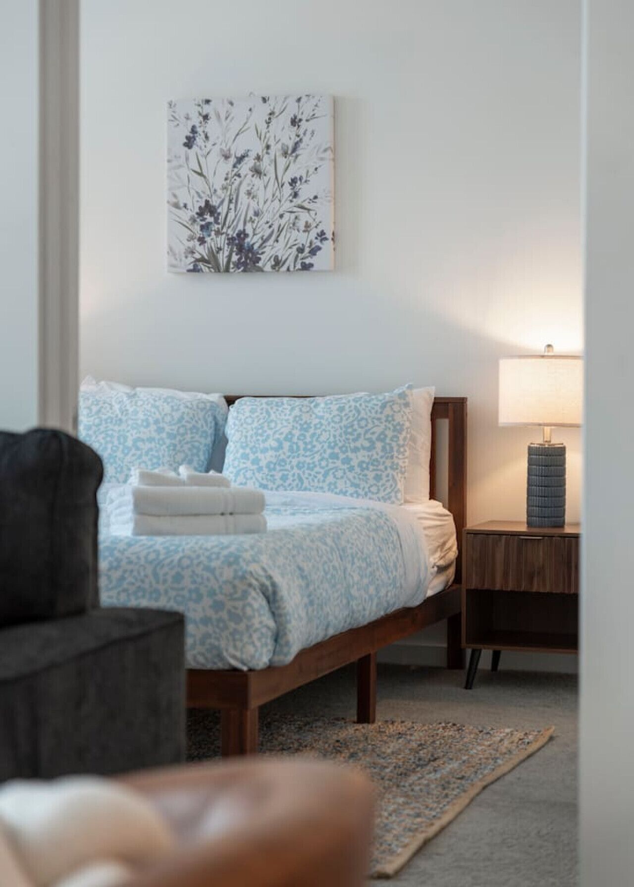 Quarto com cama, mesa de cabeceira, luminária e obra de arte na parede.