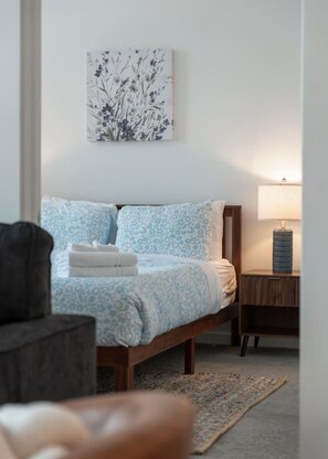A bedroom with a bed, a nightstand, a lamp, and a wall-mounted artwork.
