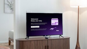 Un soggiorno moderno con una TV a schermo piatto su un mobile in legno, una lampada da terra e un divano.
