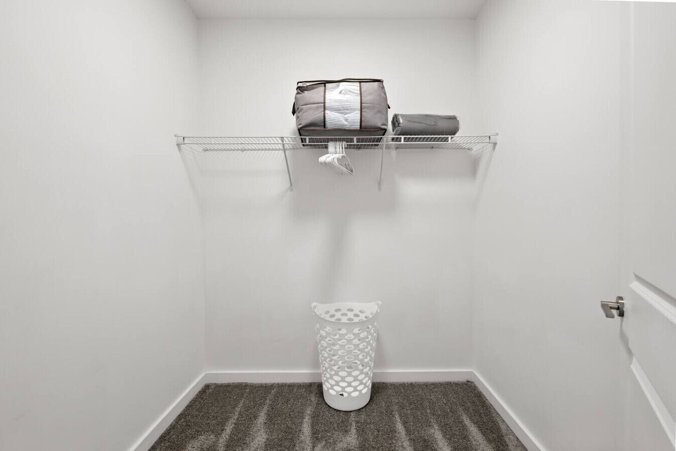 Une petite salle de bain avec des toilettes, une poubelle à motifs et une étagère en métal sur laquelle se trouvent un sac et un objet enroulé.