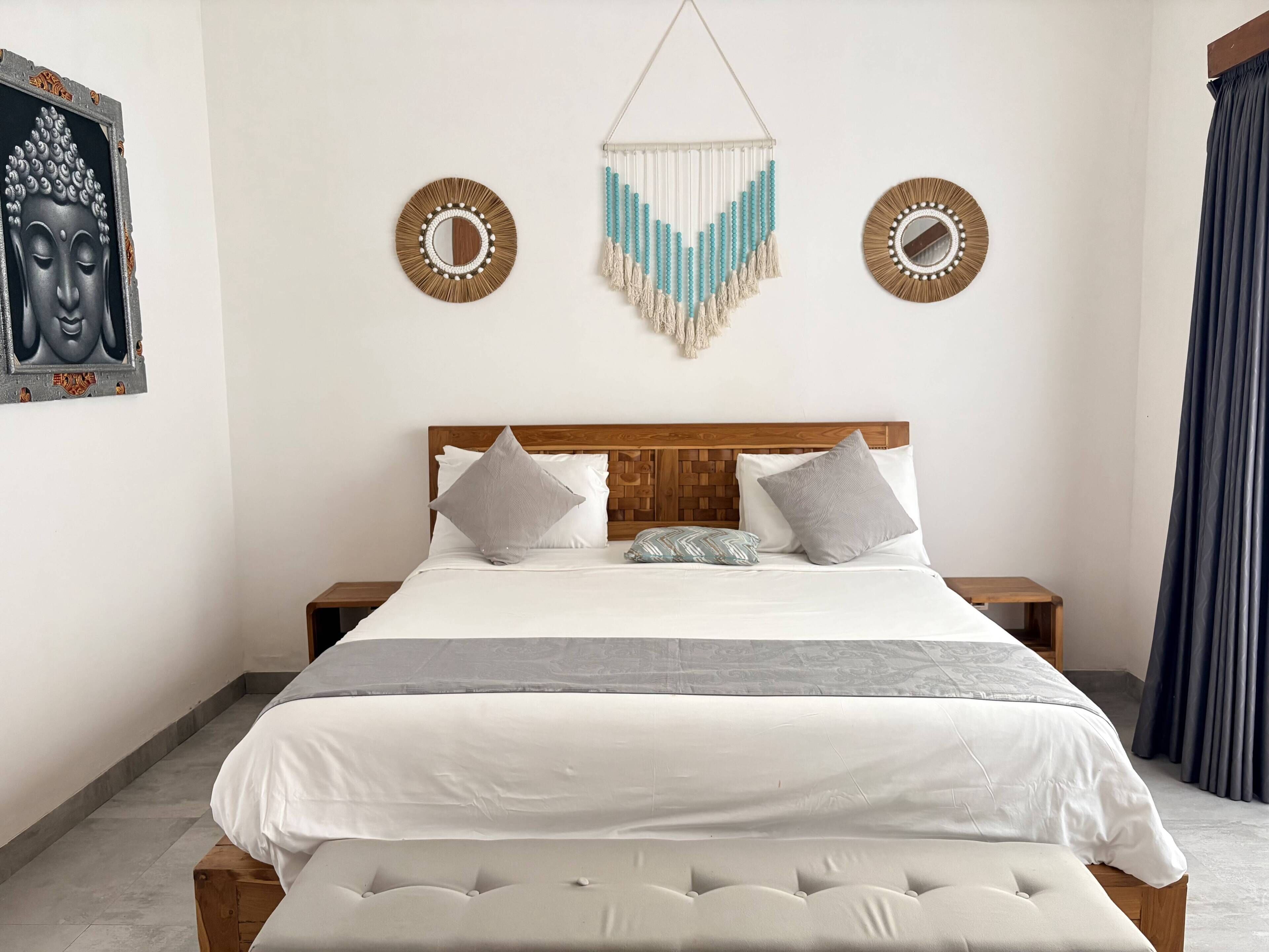 A bedroom with a bed, two nightstands, a wooden headboard, a wall hanging, and a window with curtains.