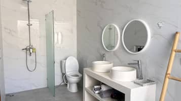 Une salle de bain moderne dotée d’une douche à parois de verre, de toilettes, de deux miroirs ronds et d’un meuble-lavabo avec un évier.