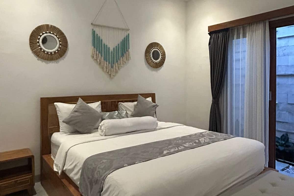 Ein Schlafzimmer mit einem großen Bett, Nachttischen und Blick ins Freie durch ein Fenster mit Vorhängen.