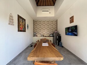 Un comedor con una larga mesa de madera, sillas, una cocina al fondo y un televisor en la pared.
