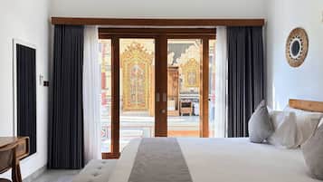 Habitació d'hotel amb un llit gran, un panell de capçalera de fusta, una taula i vista a una porta ornamentada a través de les portes corredisses.