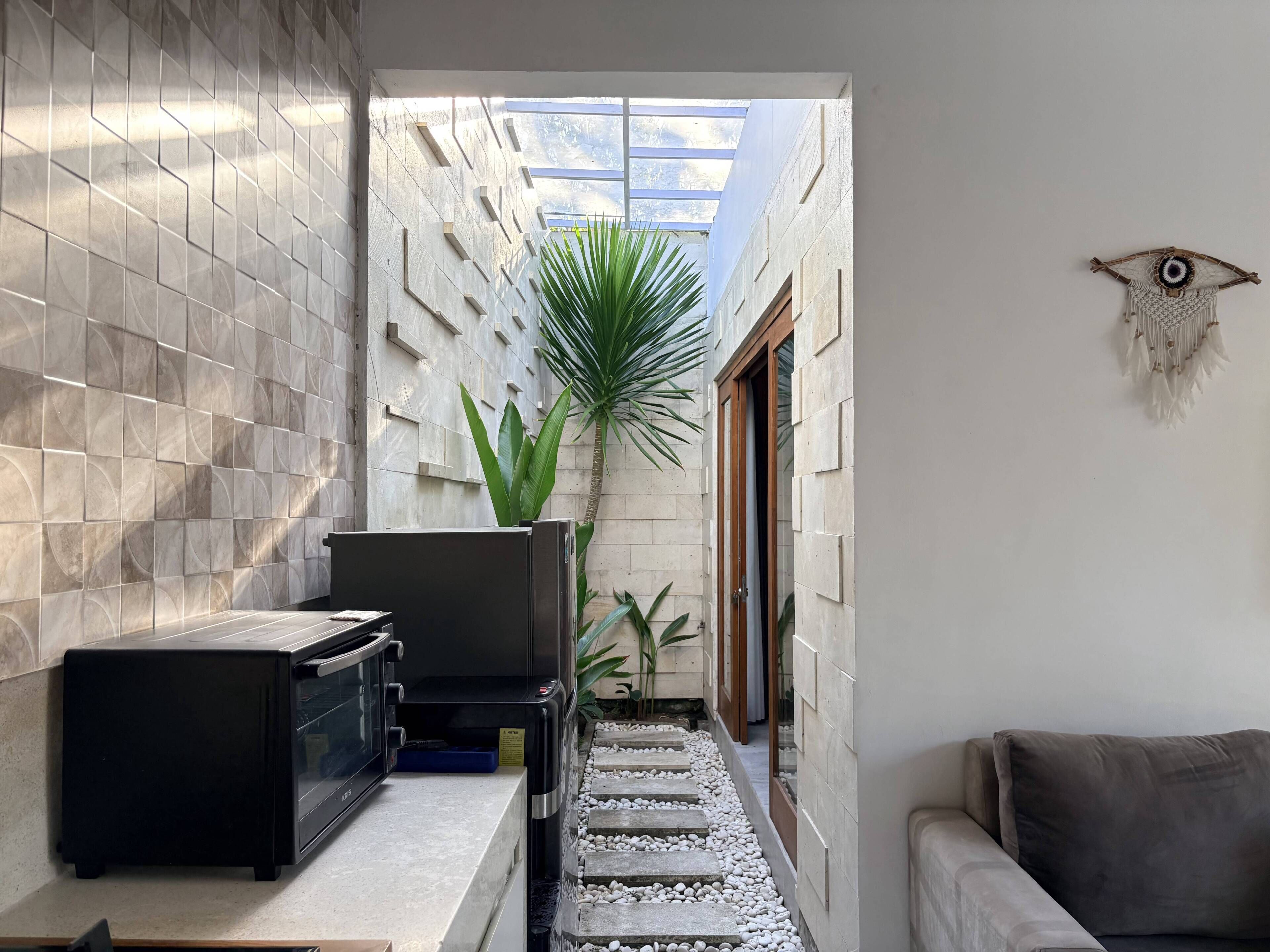A narrow hallway with a tiled wall, a microwave, a plant, and a couch.