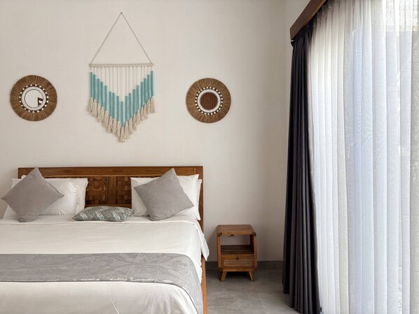 Una cama bien hecha con cabecera de madera, dos elementos decorativos en la pared y una mesita de noche de madera.