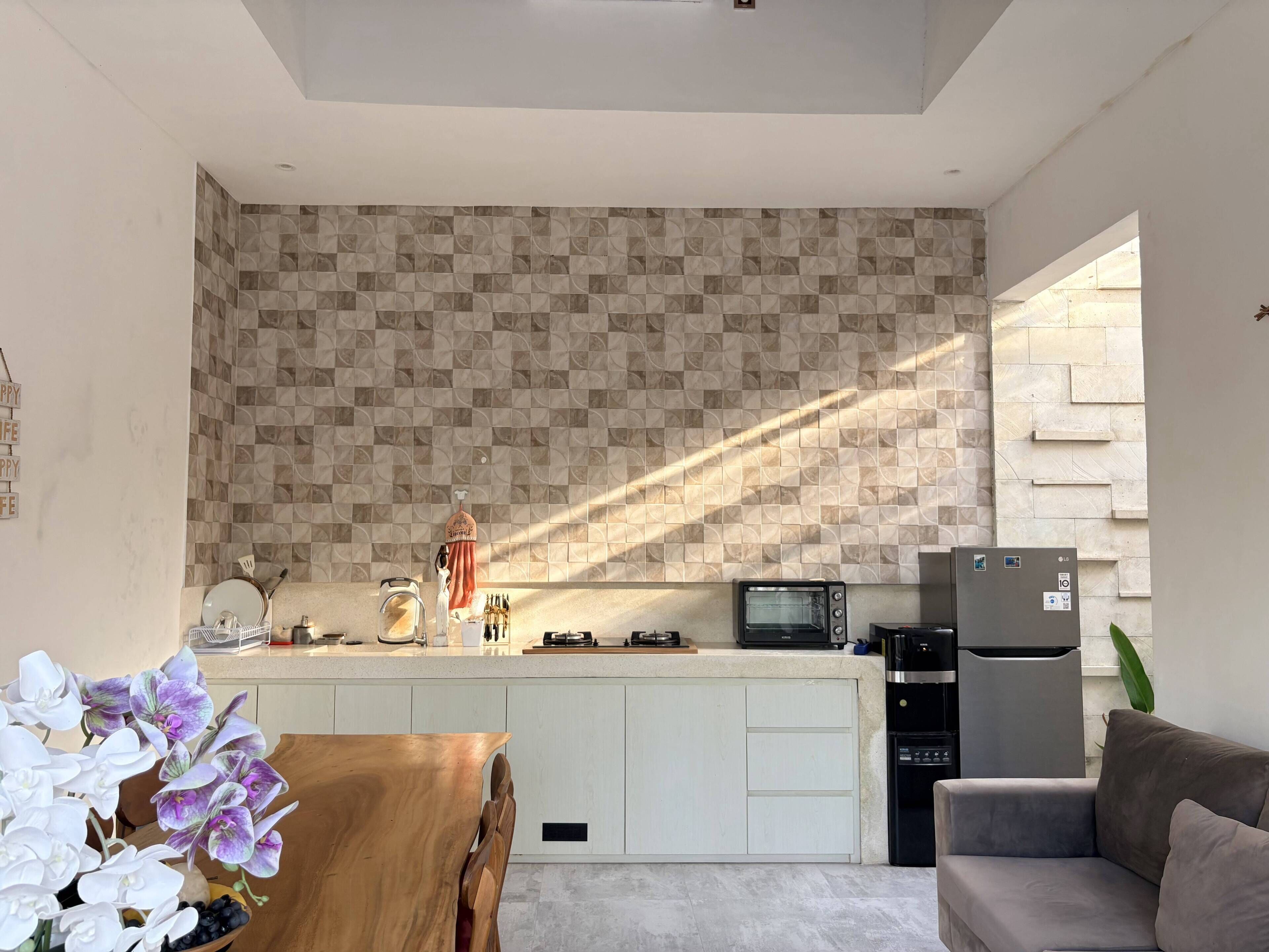 A modern kitchen with a patterned backsplash, a built-in microwave, a refrigerator, and a dining area with a wooden table and chairs.