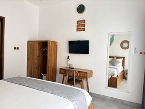 A bedroom with a bed, a wooden wardrobe, a desk with a chair, a television, and a mirror reflecting the bed. - Amy Guesthouse Nusa Dua (Nusa Dua)