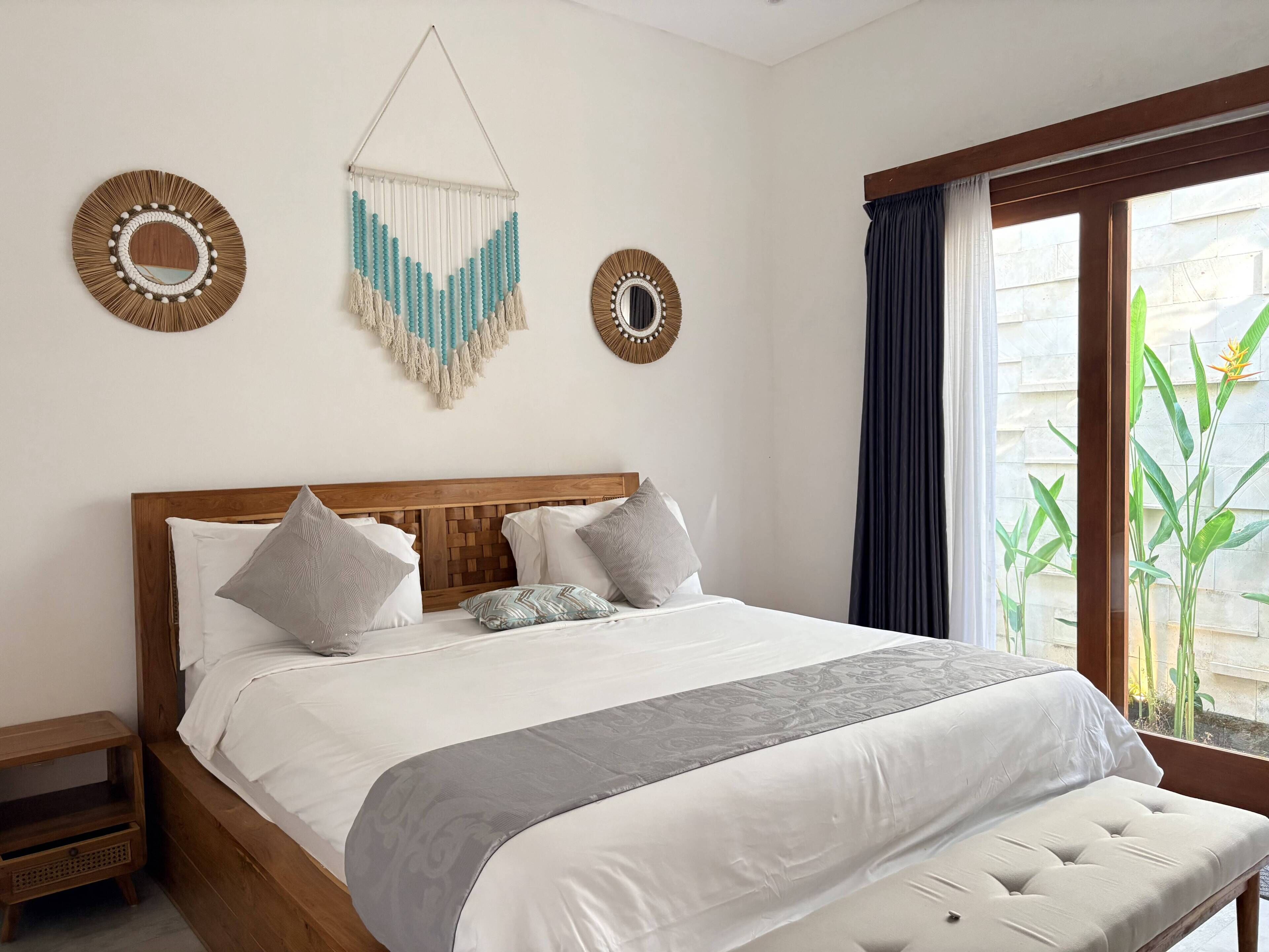 Une chambre d’hôtel avec une tête de lit en bois, un grand lit avec une literie blanche, deux tables de chevet et une fenêtre avec des rideaux.