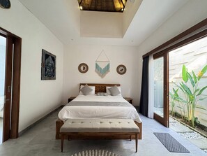 A bedroom with a bed, bedside tables, a wall-mounted mirror, and a window with a view of greenery. - Amy Guesthouse Nusa Dua (Nusa Dua)