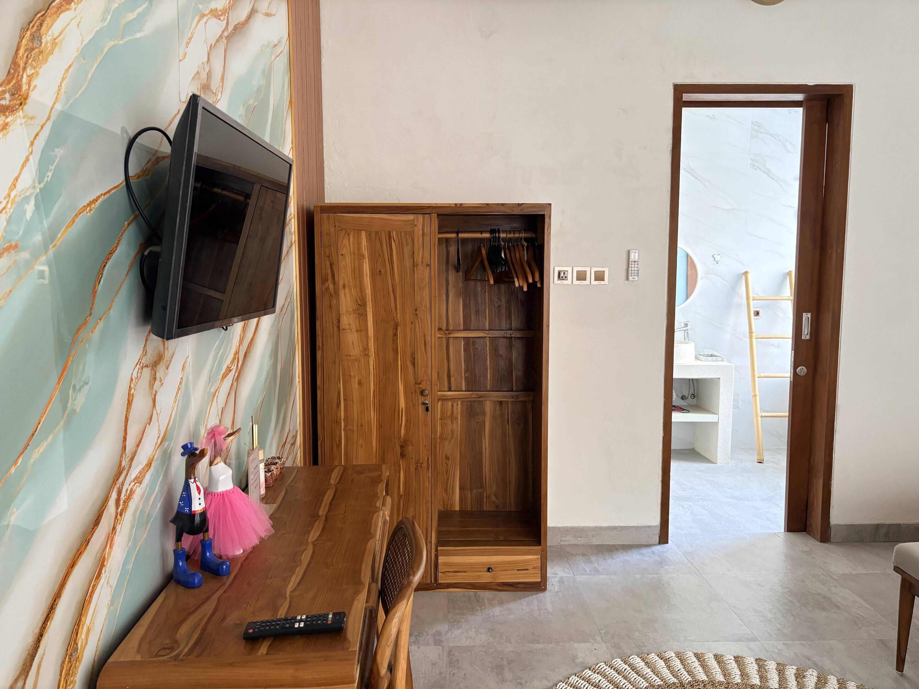 A room with a wooden TV stand, a wooden wardrobe, a remote control, and a small figurine on the wall.