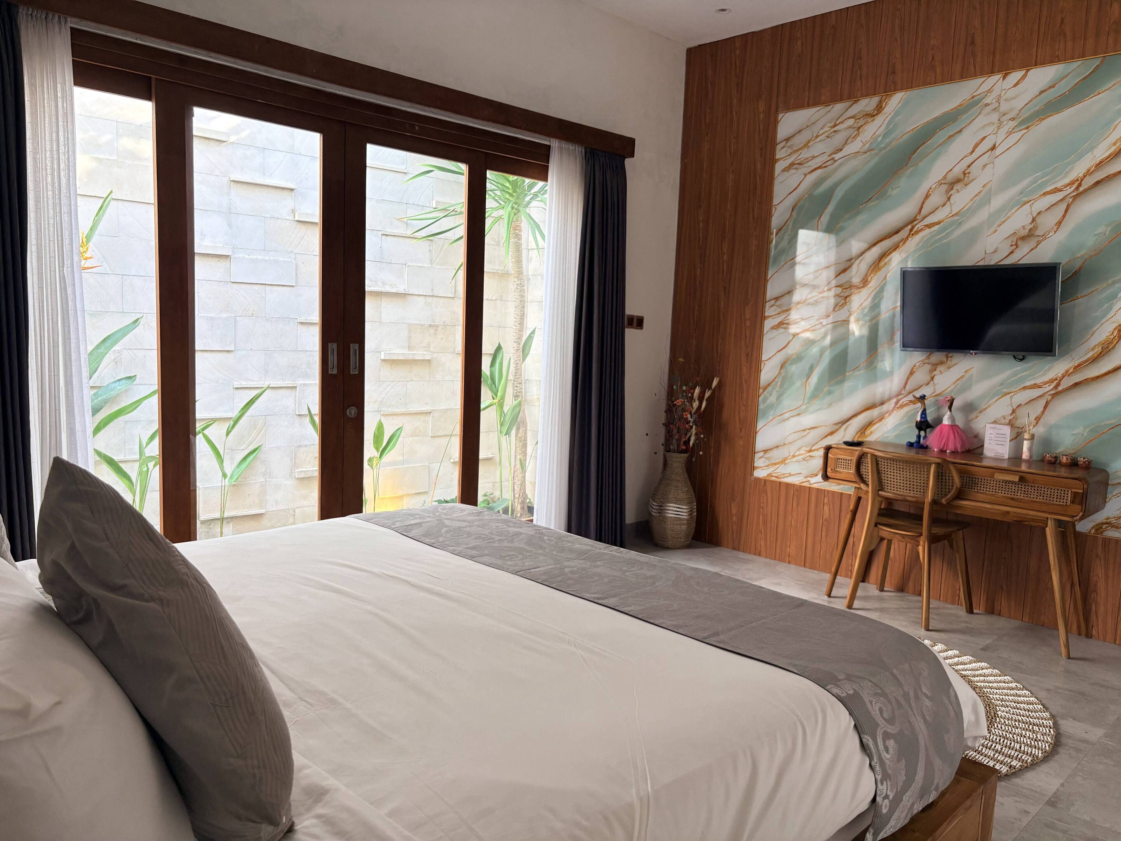 A hotel room with a bed, a desk, a television, and a view of the outside.