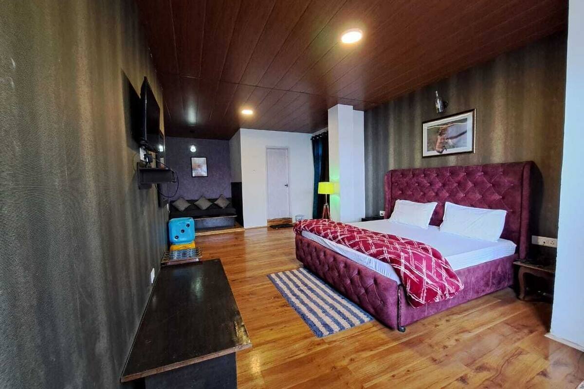 Une chambre avec un grand lit, un plancher en bois, un bureau et un téléviseur.