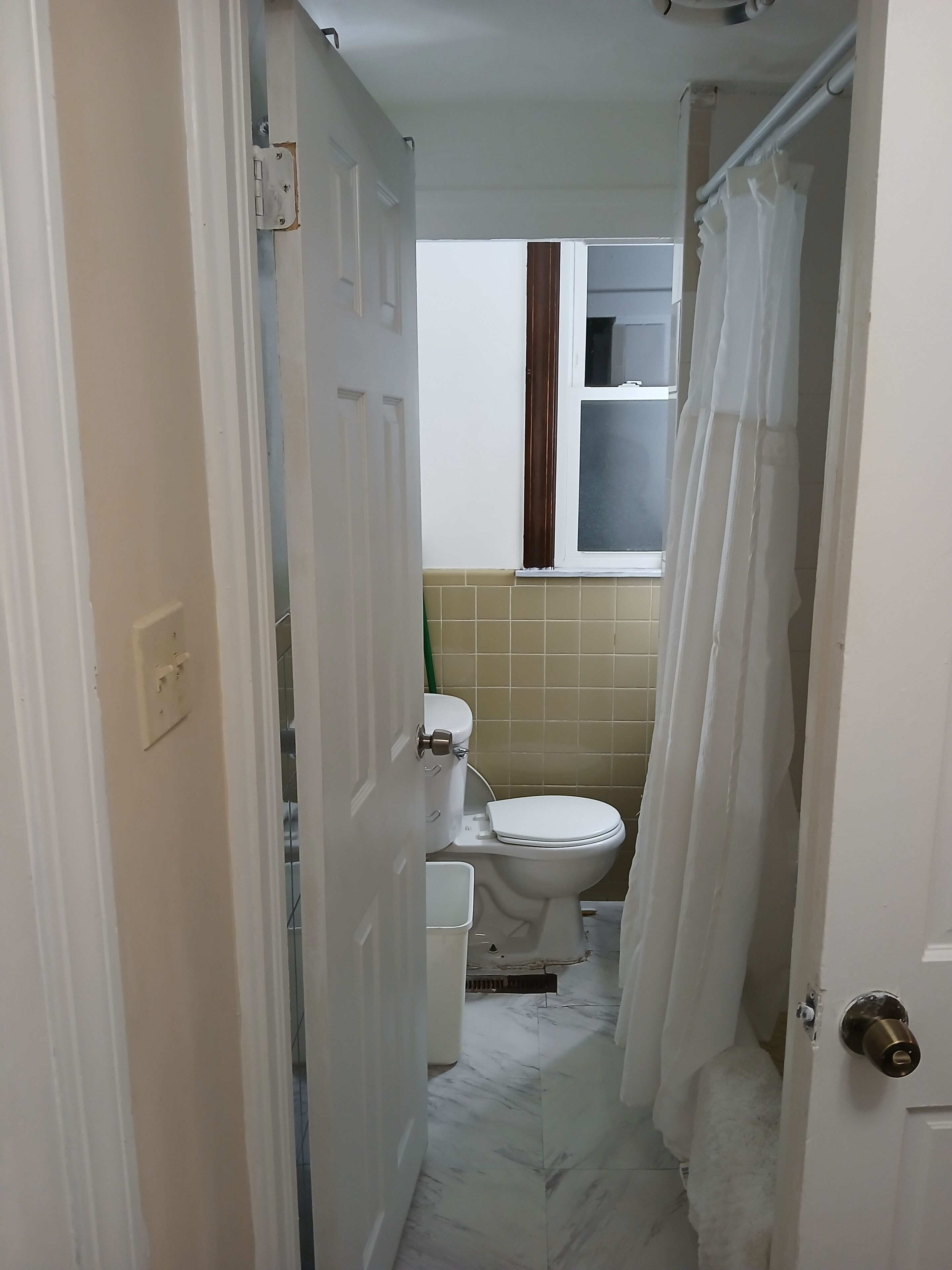 Un bagno stretto con il water, una tenda della doccia e un pavimento piastrellato.