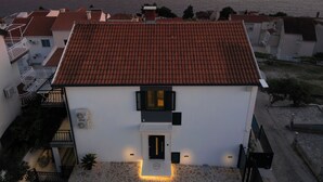 A two-story building with a red-tiled roof, a stone facade, and a small entrance with a door.