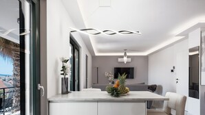 A modern kitchen with a central island, a dining area with a sofa, and a large window offering a view of the city.