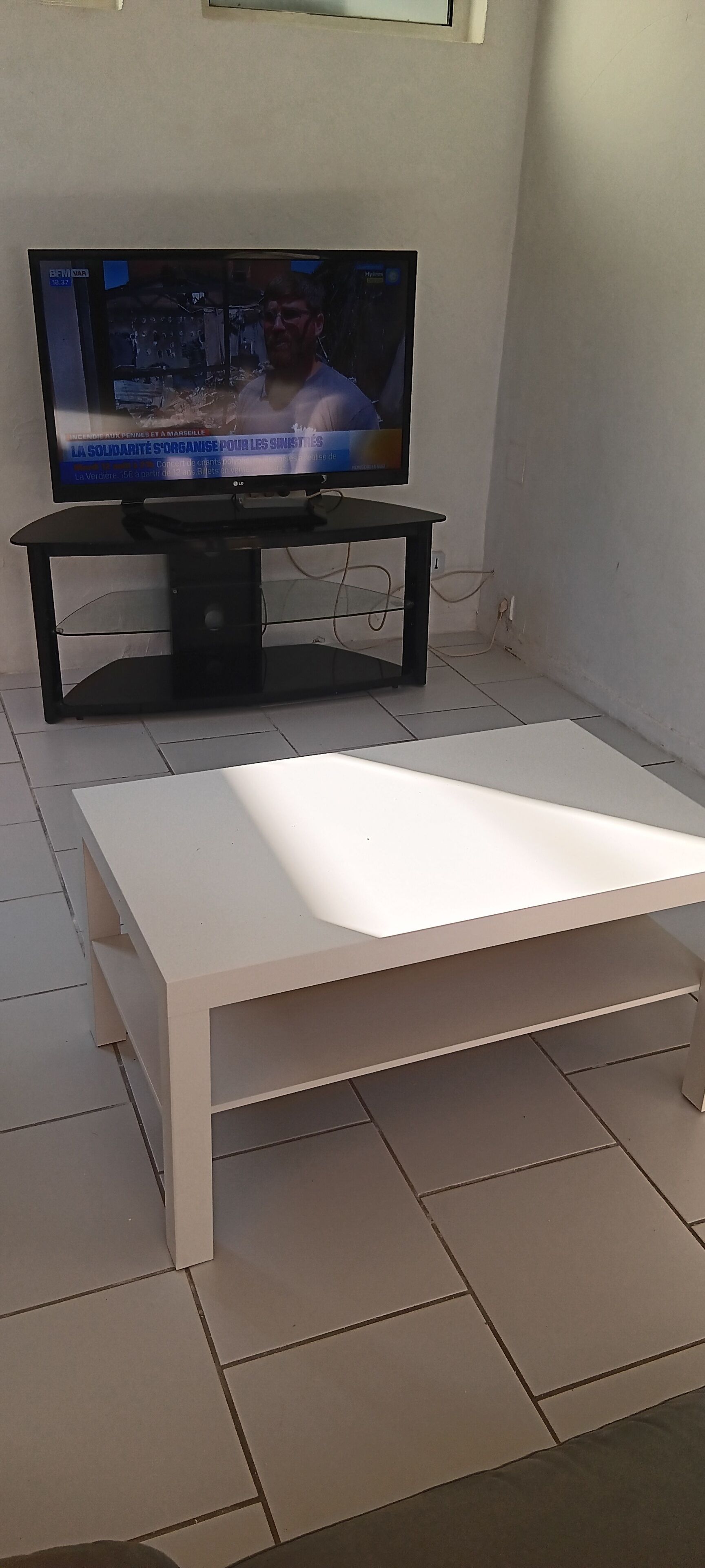 A modern living room with a flat-screen TV on a black stand, a white coffee table, and tiled flooring.