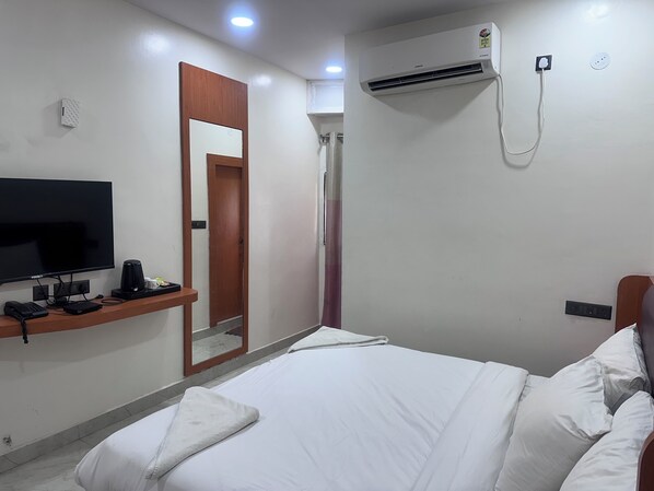 A hotel room with a bed, a TV, a mirror, an air conditioning unit, and a shower.