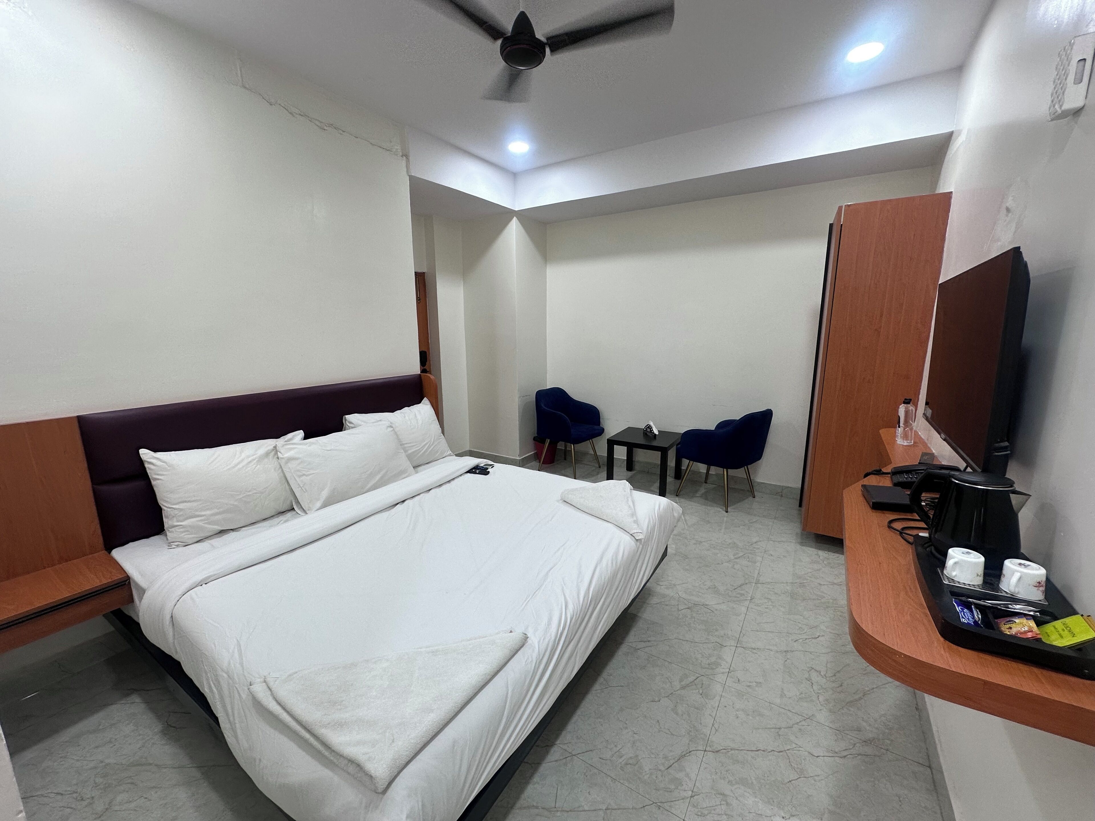 A hotel room with a bed, a desk with a chair, a small table, a mirror, and a coffee machine.