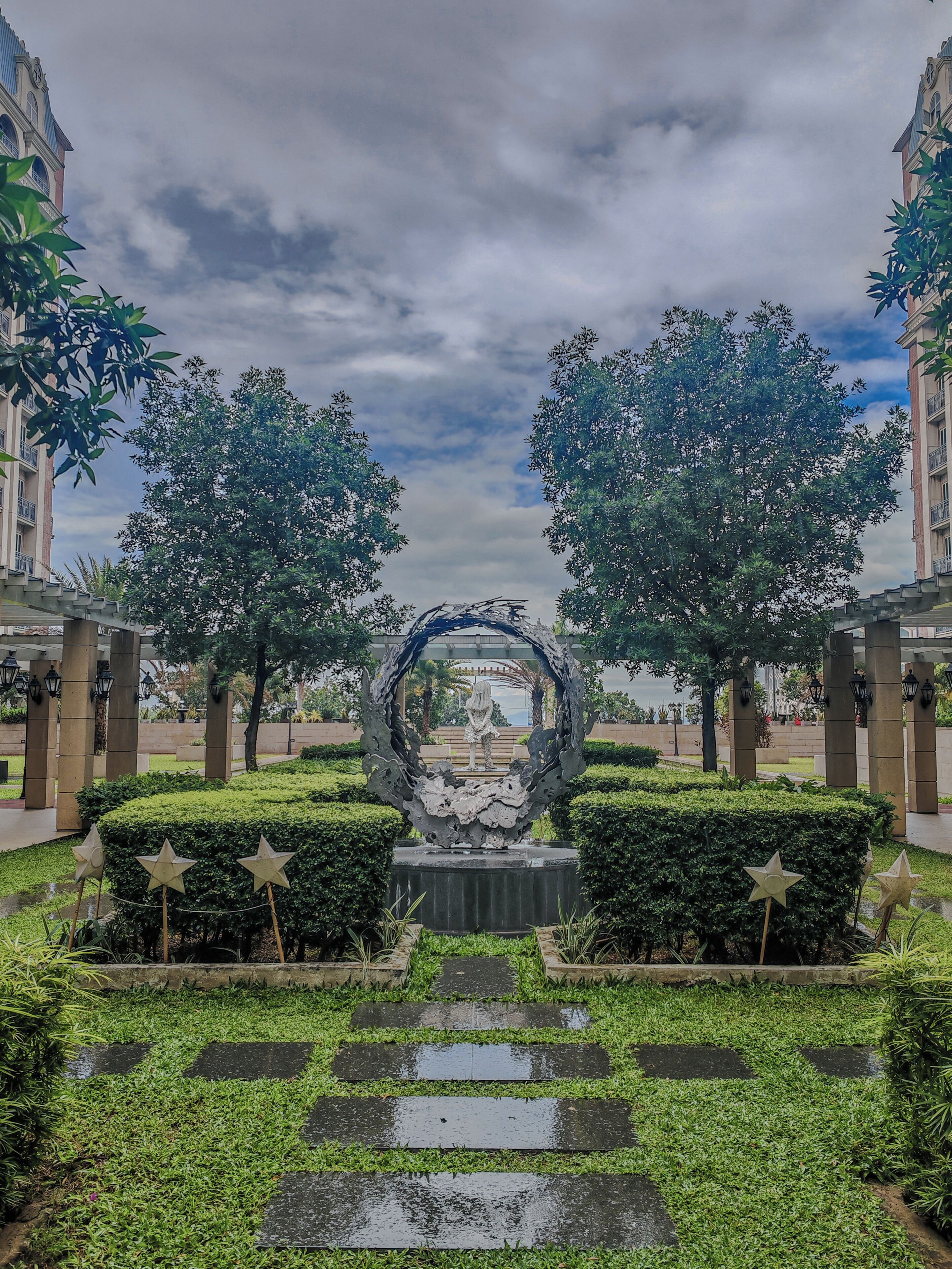 Un sendero que lleva a una escultura central rodeada de árboles y un edificio.