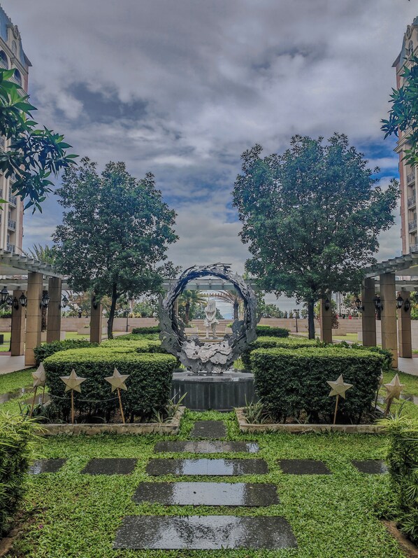 Un chemin menant à une sculpture centrale, entourée d’arbres et d’un bâtiment.