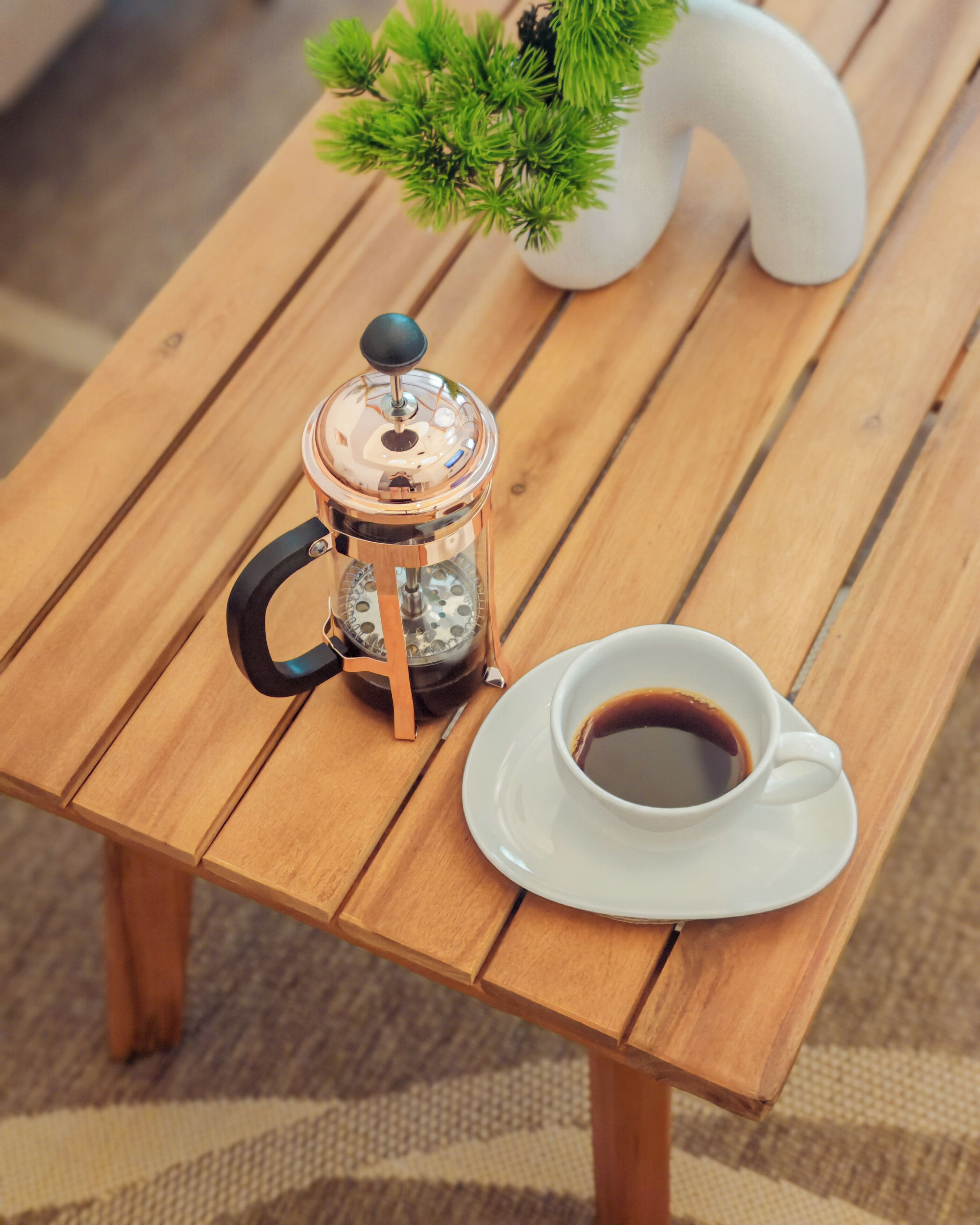 A wooden table with a coffee pot and a cup of coffee.