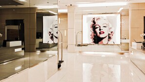 A modern hotel lobby with a glossy tiled floor, a reception desk, and a large mural of a woman.